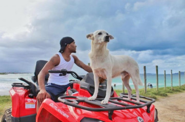 Menino com seu cachorro branco em quadriciclo vermelho andando em Arraial do Cabo