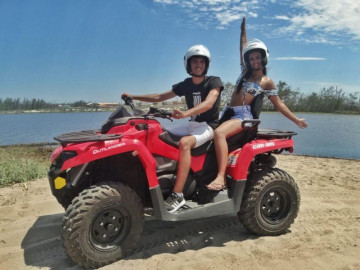 Dois jovens curtindo férias na praia de Arraial do Cabo, andando de quadriciclo próximo ao mar
